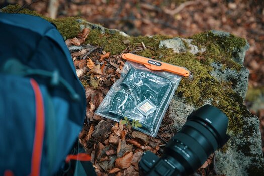 Gefüllte HERMETIC dry bag liegt auf Fels mit Herbstblättern umgeben von Kamera und Rucksack