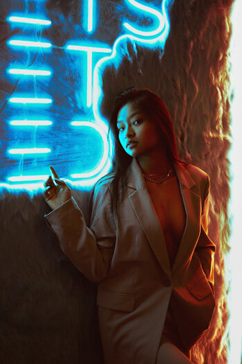 Model lehnt an Wand in dunkler Location vor blauem Neonschriftzug. Beispielbild mit dem Effektfilter Black Mist