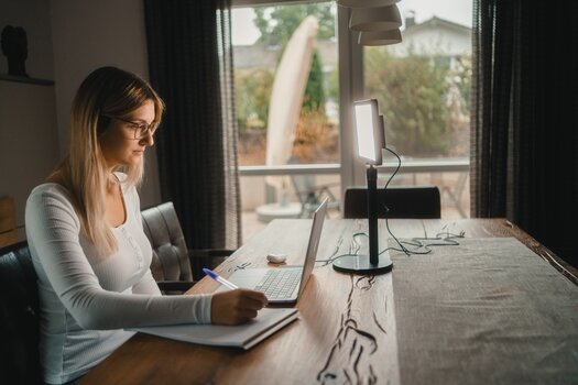 Frau sitzt in Wohnumgebung an einem Tisch vor einem Laptop und macht sich Notizen. Links neben dem Laptop das Lumis Key Pro Light Frau sitzt in Wohnumgebung an einem Tisch vor einem Laptop und macht sich Notizen. Links neben dem Laptop das Lumis Key Pro Light