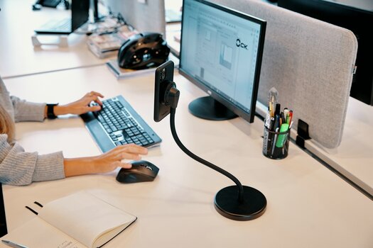 seitlicher Blick auf einen Schreibtisch mit Monitor, Tastatur und Vacuum flex desk base mit montiertem Smartphone
