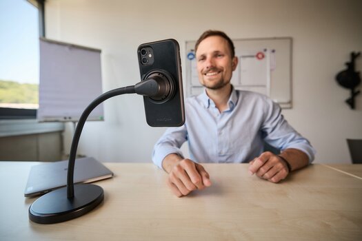 Mann sitzt am Schreibtisch, vor sich das Smartphone auf dem Vacuum flex desk base montiert