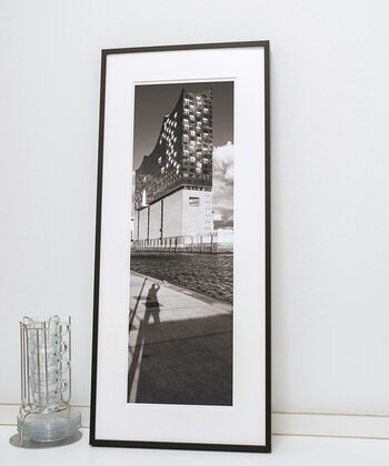 Schwarzweissfoto der Elbphilharmonie in Hamburg im Hochformat lehnt im schwarzen Rahmen mit weißem Passepartout an einer Wand.