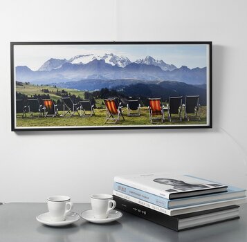 Panorama mit Liegestühlen vor Berglandschaft hängt gerahmt an einer Wand. 