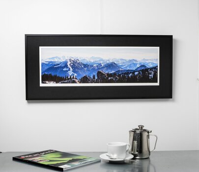 Panorama einer Berglandschaft mit schwarzem Passepartout und Rahmen hängt an einer weißen Wand.