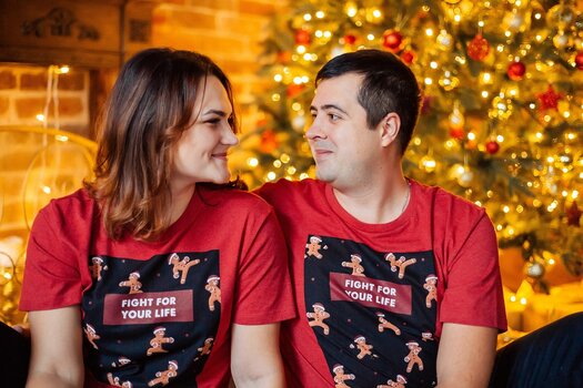 Pärchen mit gleichem Weihnachts-T-Shirt vor beleuchtetem Weihnachtsbaum