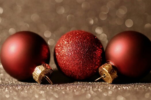 3 rote Weihnachtskugeln liegen auf glitzerndem Untergrund nebeneinander. 