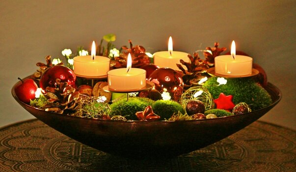4 Teelichter in einer Schale, die mit mit Moos, Kieferzapfen, Weihnachtsdekoration gefüllt ist. 