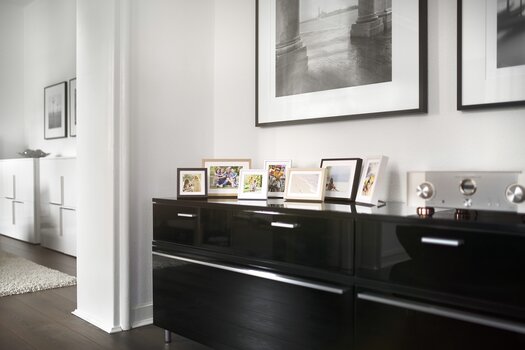 Verschiedene Bilder in kleinen Fotorahmen sind auf einem schwarzen Sideboard aufgestellt. 
