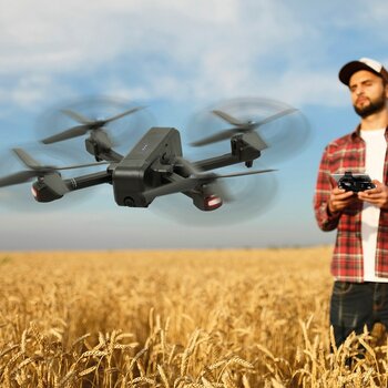 Mann steuert die Drohne fly100pro. Aufnahme in einem Getreidefeld.
