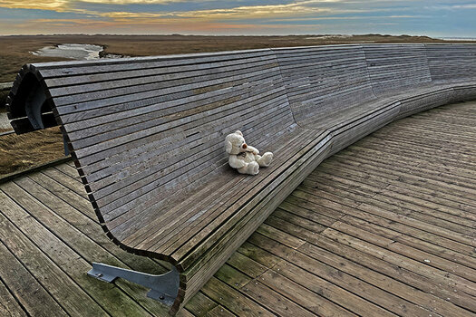 Ein Teddybär sitzt auf einer großen Holzbank am Strand