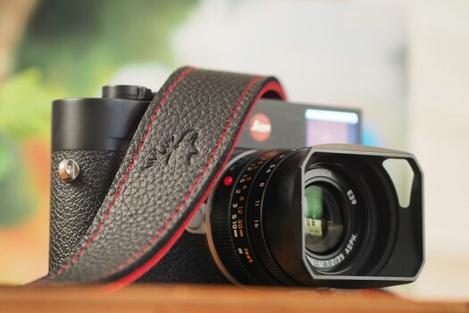 Leica Kamera seitlich von vorne mit darübergelegtem Eddycam-Kameragurt in schwarz mit roter Kontrastnaht