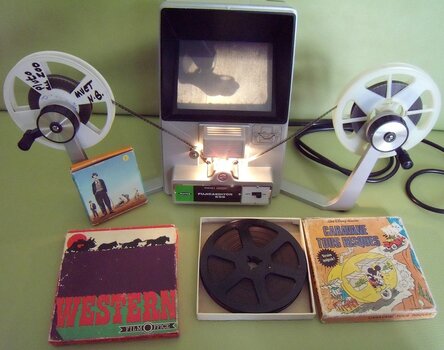 Schneidegerät für Schmalfilm, links und rechts Filmspulen. Davor alte Filmausgaben auf Schmalfilm in Kartonverpackung.