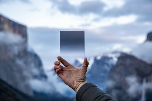 Hand hält Rechteckfilter hoch. Im Hintergrund Berglandschaft