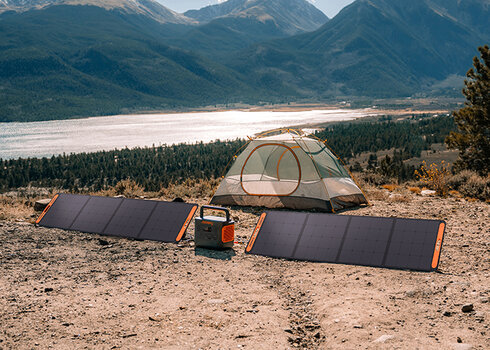 Anwendungsbeispiel: Vor einem Zelt steht der Jackery Explorer 1500 Pro, links und rechts zwei Solarpanels. Im Hintergrund beeindruckende Berg- und Seelandschaft.