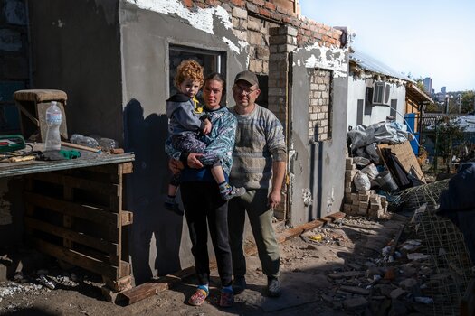 Marina, Sergii und ihr Sohn vor ihrem Haus, das durch einen Raketeneinschlag zerstört wurde. Seitdem haben sie es wiederaufgebaut. Sie sind Mandanten des IRC-Rechtsprogramms. © The International Rescue Committee. Foto: Diana Zeyneb Alhindawi für das IRC