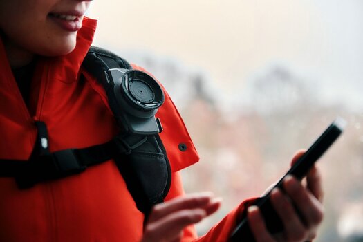 Frau mit roter Jacke hat Vacuum tex base an Rucksackgurt in Schulterhöhe befestigt