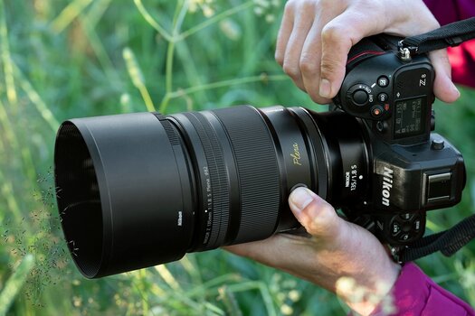 Hände halten Nikon-Kamera mit angesetztem  NIKKOR Z 135 mm f/1.8 S Plena