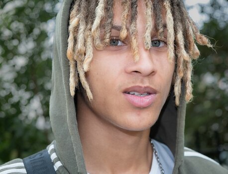 Intensives Porträt eines jungen Mannes mit hellen Augen und Dreadlocks unter einer Kapuze.