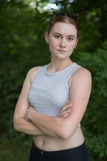 Porträt einer jungen Frau mit verschränkten Armen vor grünem Hintergrund, das Entschlossenheit ausstrahlt.