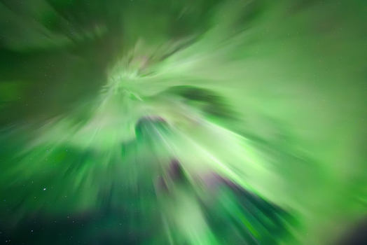 Astrofotografie einer Polarlicht-Corona mit strahlenförmig auseinanderlaufenden grünen Lichtbändern direkt im Zenit.