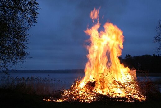 Großes Maifeuer am Seeufer in der Dämmerung mit spiegelndem Wasser