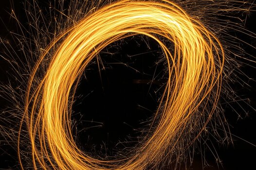 Goldene Lichtspuren in Kreisform durch Lightpainting mit einer Wunderkerze oder Taschenlampe vor schwarzem Hintergrund bei Nacht.