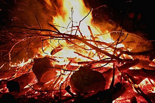 Loderndes Feuer mit glühenden Holzscheiten und Funkenflug bei Nacht