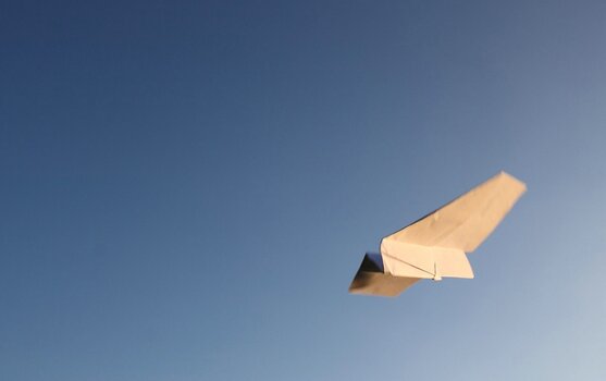 Papierflieger im Flug vor klarem blauem Himmel