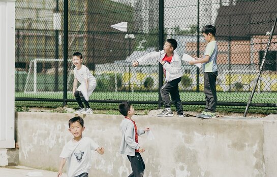 Kinder werfen Papierflieger auf einem Sportplatz im Freien