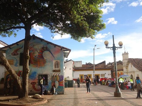 Straßenszene im historischen Viertel La Candelaria in Bogotá mit farbenfroher Wandkunst, kolonialer Architektur und Menschen auf einem Platz.