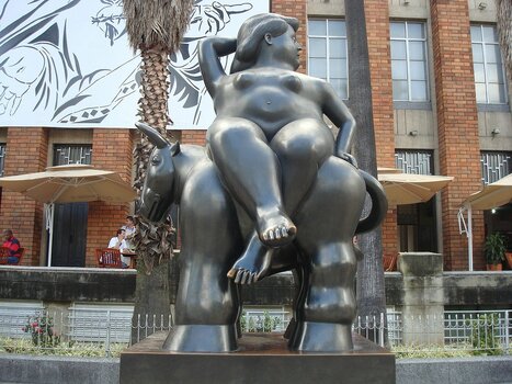 Bronzeskulptur von Fernando Botero auf der Plaza Botero in Medellín vor urbaner Kulisse und moderner Straßenkunst.
