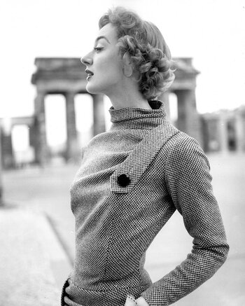 Schwarz-weiße Modefotografie von F.C. Gundlach aus dem Jahr 1955: Ein Model steht elegant gekleidet vor dem Brandenburger Tor in Berlin (West) und symbolisiert die Aufbruchsstimmung der Nachkriegsjahre.