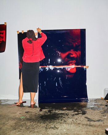 Akosua Viktoria Adu-Sanyah arbeitet an einer großformatigen fotografischen Installation mit roten und dunklen Farbschichten in einem Ausstellungsraum.