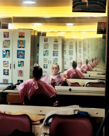 Farbfotografie aus „Rotting from Within“ mit Spiegelungen in einem Friseursalon, die Identität, Selbstbild und familiäre Zugehörigkeit thematisiert. Farbfotografie aus „Rotting from Within“ mit Spiegelungen in einem Friseursalon, die Identität, Selbstbild und familiäre Zugehörigkeit thematisiert.