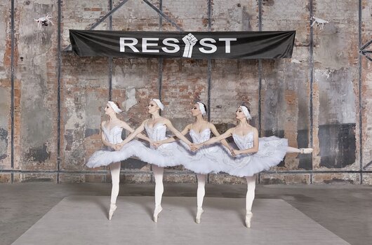 Ballerinen posieren vor einem großen „RESIST“-Banner neben Polizeikräften in Halil Altınderes Arbeit „Ballerinas and Police“.