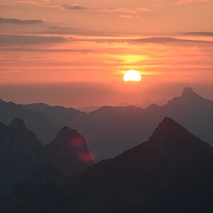 Sonnenaufgang über Voralpen. Unterhalb der Sonnenscheibe beugt sich das Rot des Himmels unnatürlich hinunter.