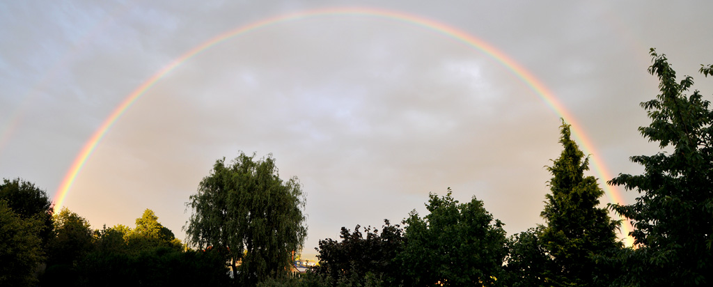 Ein vollständiger Regenbogen, zusammengesetzt aus zwei aus der Hand geschossenen Bildern.