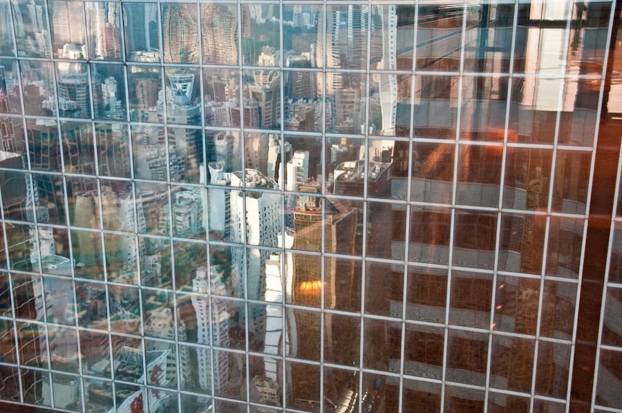 Skyline von Hong Kong verspiegelt vom gegenüberliegendem Gebäude, fotografiert durch eine Scheibe.