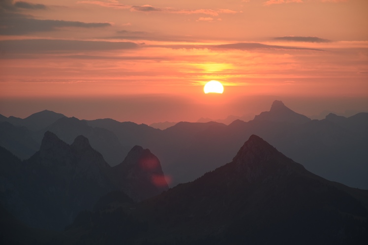 Sonnenaufgang über Voralpen. Unterhalb der Sonnenscheibe beugt sich das Rot des Himmels unnatürlich hinunter.