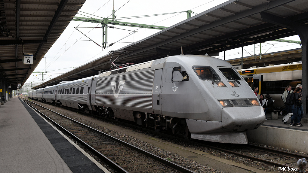 Das Bild zeigt den grauen Motorwagen eines siebenteiligen Elektrotriebwagens am Bahnsteig. Die Front ist abgeflacht. Vier Scheinwerfer leuchten in einer trapzförmigen Anordnung.
