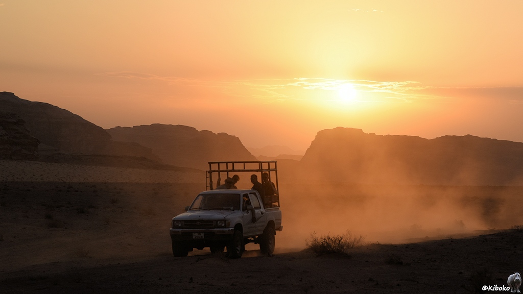 Weißer Geländewagen in oranger Staubwolke bei Sonnenuntergang