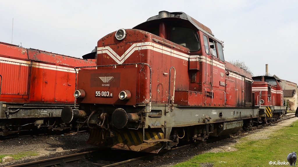 Das Bild zeigt eine vierachsige, rote Diesellokomotive mit zwei weißen Streifen und grauem Rahmen.