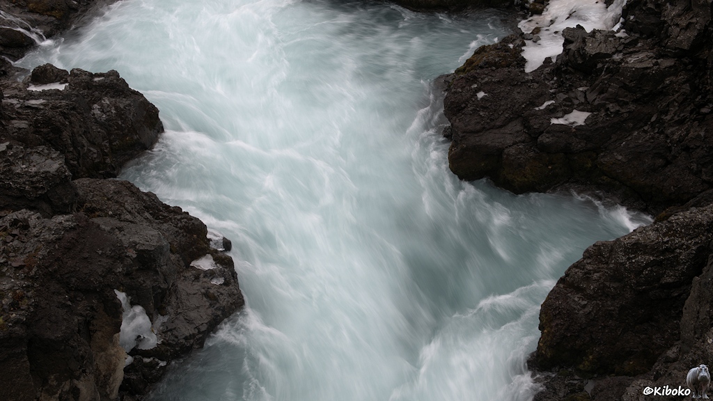 Blick und von einer Brücke in eine enge Schlucht. Zwischen dunklen Felsen läuft schäumend ein Fluss durch.