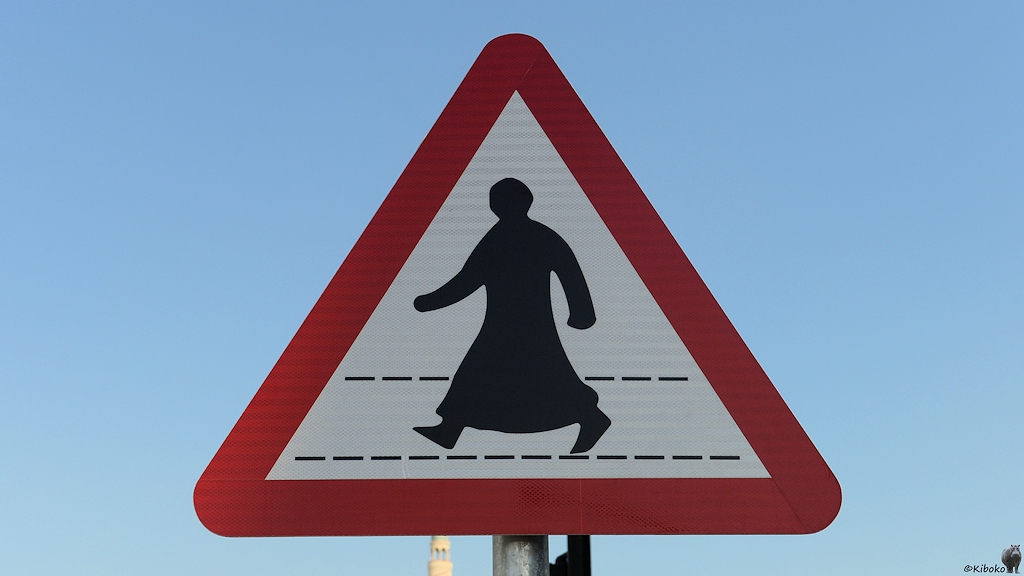 Das Bild zeigt ein dreieckiges Schild mit der Spitze nach oben und rotem Rand. Darauf ist ein schwarzer Mann im langen Gewandt, der auf einer gestrichelten Linie läuft, auf weißem Grund.