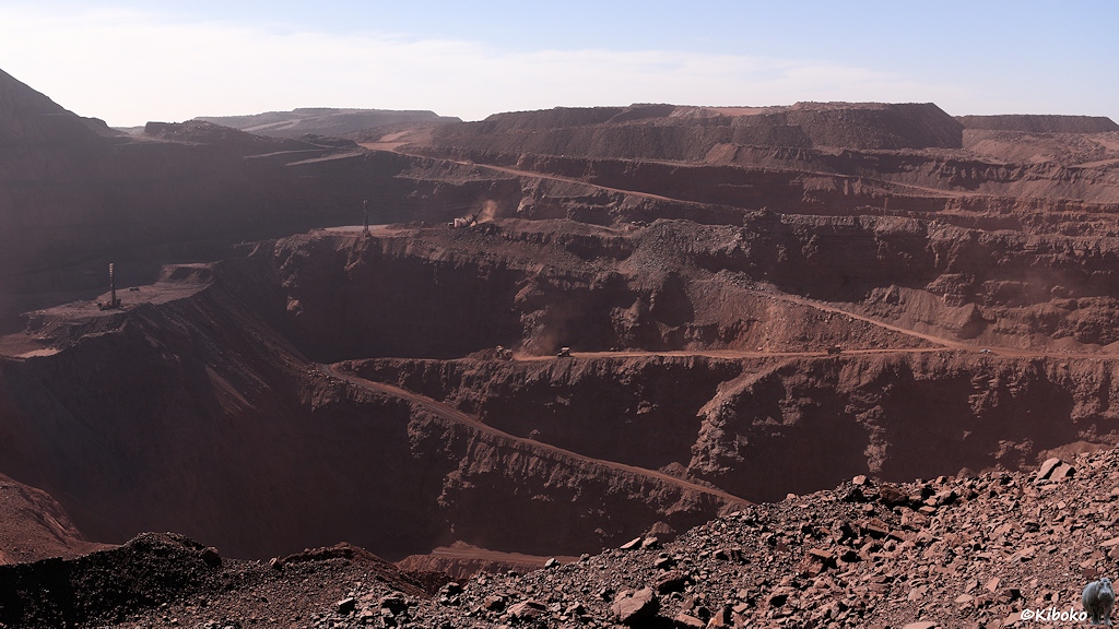 Blick in die Eisenmine. Eine Straße führt im Zickzack in die Tiefe. Die LKWs wirken wie Ameisen