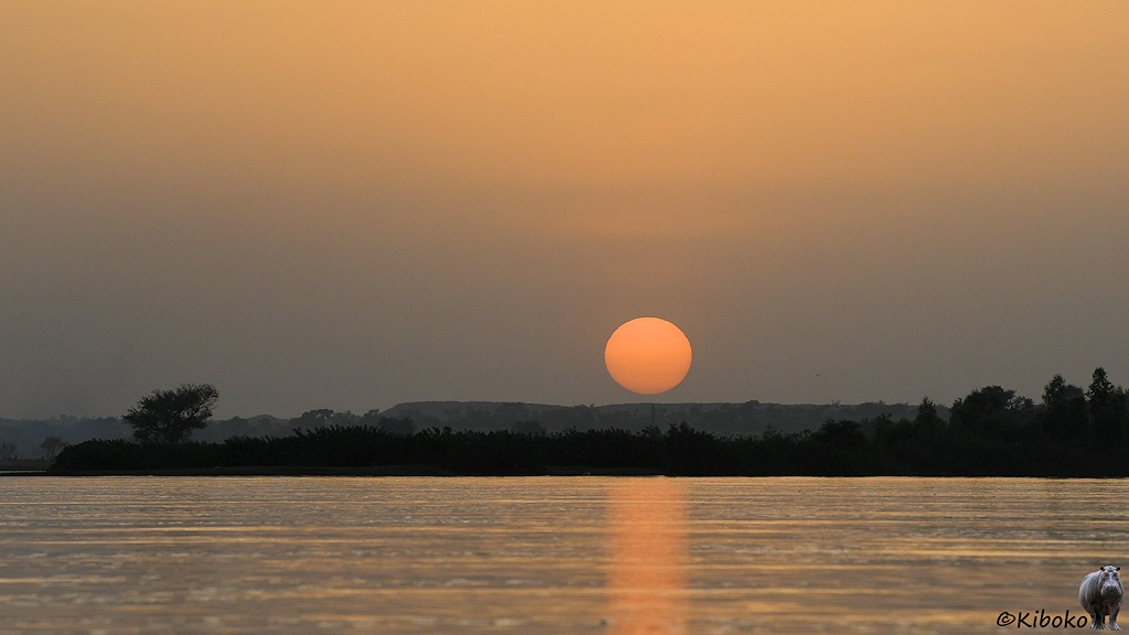 Das Bild zeigt die untergehende Sonne über Hügeln. Die Sonne spiegelt sich im Flus im Vordergrund.