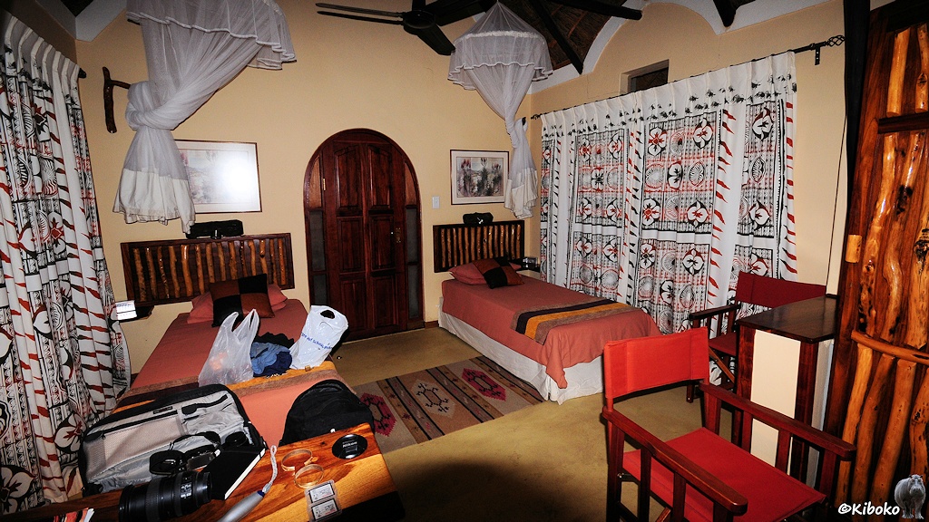 Zimmer in der Lodge mit zwei einzelnen Betten und bunten Vorhängen. Über den Betten hängen Moskitonetze.