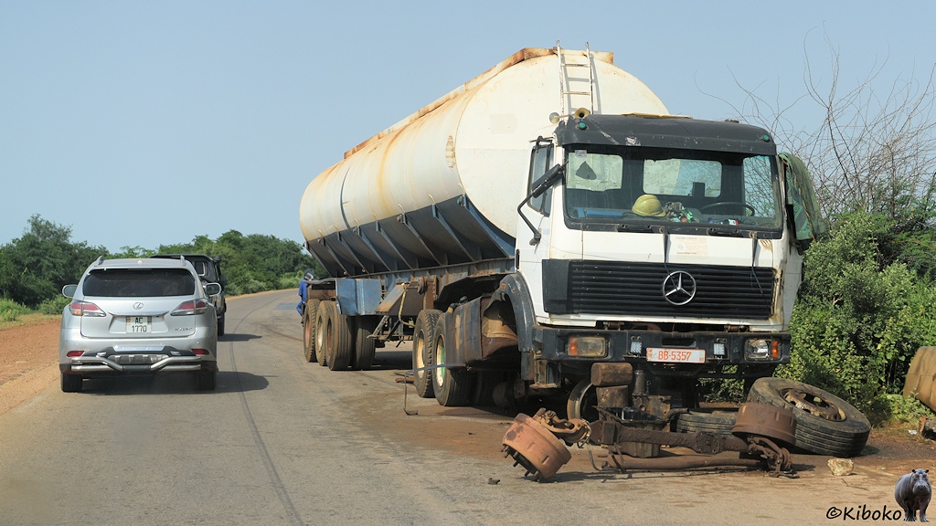 Das Bild zeigt einen weißen Mercedes LKW mit Tankauflieger am rechten Straßenrand. Der LKW ist vorn aufgebockt. Vor dem LKW liegen Vorderachse, Bremstrommeln und Räder.