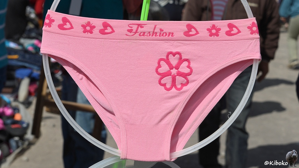 Das Bild zeigt einen rosa Damenschlüpfer mit einem Symbol aus 5 roten Herzen sowie Herzmuster am Bündchen. Auf dem Bündchen steht in roter Schrift Fashion mit Herz als I-Punkt. Der Schlüpfer ist um einen hellgrauen Plastikring gespannt.