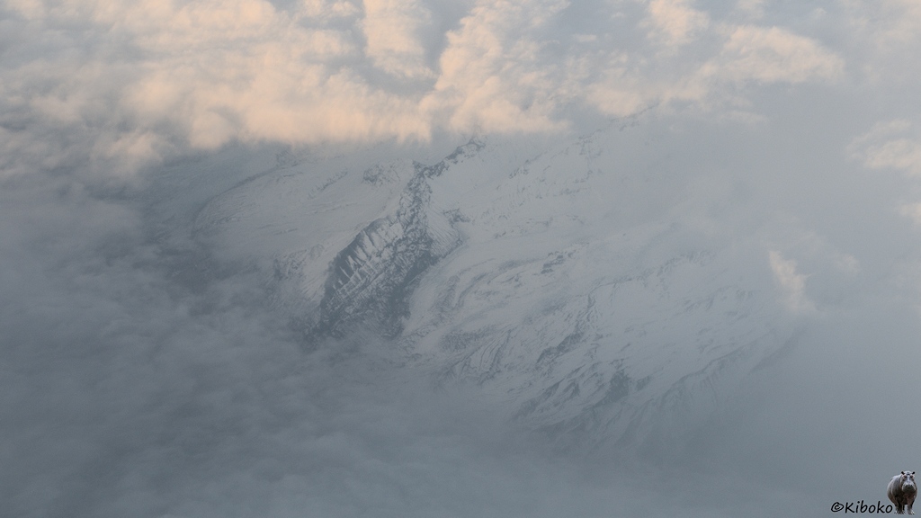 In einer Wolkenlücke liegen schneebedeckte Felsen.
